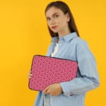 Pink laptop sleeve with a red heart pattern on a light surface. the person holding the sleeve