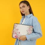 Soft beige laptop sleeve with delicate floral design in pink, green, and purple, featuring a zip closure for secure storage. the person holding the sleeve