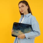 Laptop sleeve with a dark blue background featuring a starry night sky design with stars, clouds, and gradient effect. the person holding the sleeve