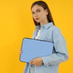 Simple blue laptop sleeve with white polka dots for a clean and stylish design. the person holding the sleeve