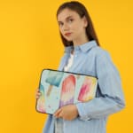 Laptop sleeve with pastel-colored popsicle design in blue, pink, purple, and peach on a light background with zip closure. the person holding the sleeve