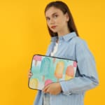 Laptop sleeve with light blue background and pastel popsicle pattern in pink, yellow, blue, and purple, featuring a zip closure. the person holding the sleeve