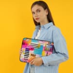 Infidu Bold Abstract Laptop Sleeve featuring bright geometric patterns in pink, blue, yellow, black, and white with a secure zip closure. the person holding the sleeve