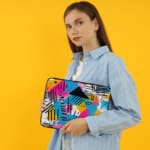 Infidu Modern Abstract Laptop Sleeve featuring bright colors like pink, blue, yellow, and black with geometric shapes and lines. the person holding the sleeve