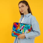 Infidu Vibrant Abstract Laptop Sleeve featuring bold colors like blue, orange, yellow, pink, and purple with geometric shapes and lines. the person holding the sleeve