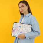 Terrazzo-style laptop sleeve with colorful spots in pink, blue, orange, and purple on a white background, the person holding the sleeve