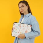 Pastel terrazzo-style laptop sleeve with pink, yellow, blue, and gray shapes on a light background, the person holding the sleeve