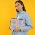 Laptop sleeve with a circular swirl pattern in pastel colors, including blue, pink, purple, yellow, and orange on a white background. the person holding the sleeve