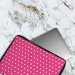 Pink laptop sleeve with a repeating white star pattern, shown against a bright background. The laptop sleeve covers the laptop