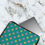 Playful pastel polka dot design laptop sleeve with yellow, purple, and orange dots on a teal background. The laptop sleeve covers the laptop