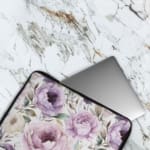 Infidu Elegant Purple Floral Laptop Sleeve featuring large purple flowers and green leaves on a light-colored background. The laptop sleeve covers the laptop