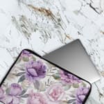 Infidu Elegant Floral Laptop Sleeve with purple and pink flowers, green leaves, and a soft white background, offering stylish laptop protection. The laptop sleeve covers the laptop