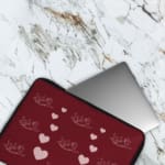 Infidu Maroon Heart & Angel Pattern Laptop Sleeve with white hearts and angel figures on a maroon background. The laptop sleeve covers the laptop