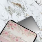 Floral laptop sleeve with pink and white flowers, black-bordered edges, soft background, and delicate floral design. The laptop sleeve covers the laptop