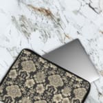 Laptop sleeve with elegant white floral and leaf motifs on a black background, featuring durable fabric and a secure zip closure. The laptop sleeve covers the laptop