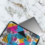 Infidu Modern Abstract Laptop Sleeve featuring bright colors like pink, blue, yellow, and black with geometric shapes and lines. The laptop sleeve covers the laptop