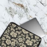 Infidu Black & Gold Floral Laptop Sleeve with a black background and detailed white floral pattern, featuring a secure zip closure. The laptop sleeve covers the laptop