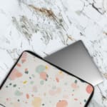 Pastel terrazzo-style laptop sleeve with pink, yellow, blue, and gray shapes on a light background, The laptop sleeve covers the laptop