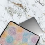 Laptop sleeve with a circular swirl pattern in pastel colors, including blue, pink, purple, yellow, and orange on a white background. The laptop sleeve covers the laptop