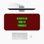 Infidu Always Be Kind To Yourself Desk Pad featuring bright green text on a maroon background, perfect for promoting self-care at your desk. A desk pad under the computer