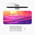 Infidu Calming Sunset Reflection Design Desk Pad featuring a sunset over water in soft shades of pink, purple, orange, and yellow. A desk pad under the computer