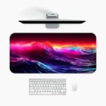 Infidu Neon Ocean Waves Design Desk Pad with vibrant shades of pink, purple, blue, and orange depicting ocean waves and sunset. A desk pad under the computer