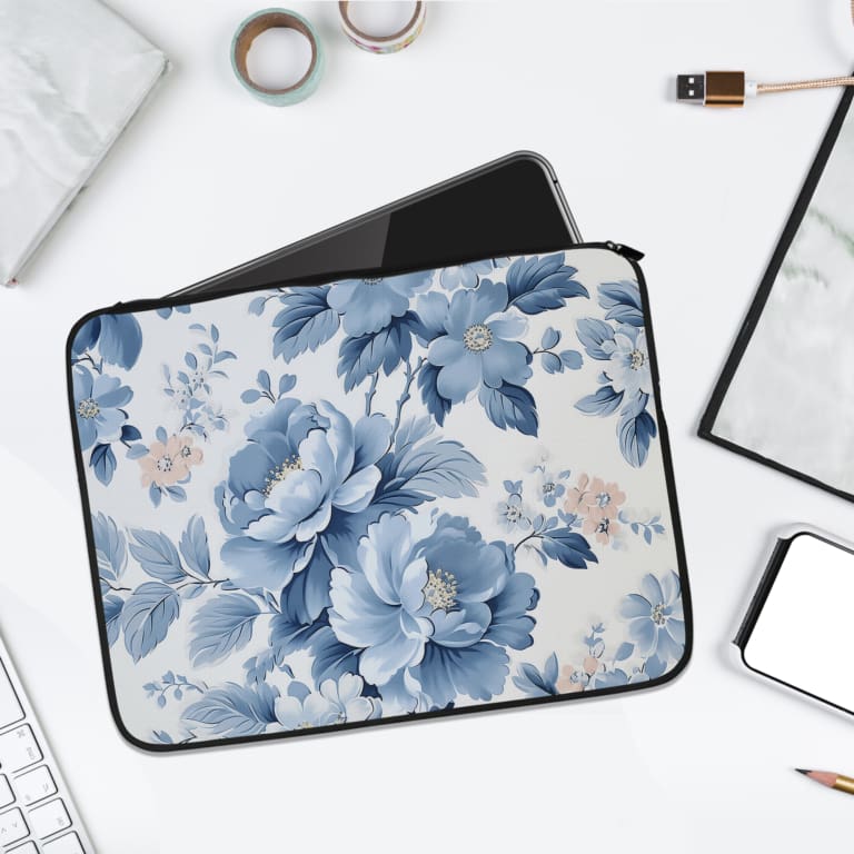 Laptop sleeve with a blue floral design, featuring light and dark blue flowers on a white background with a secure zip closure. laptop sleeve kept on a plain white background