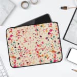 Laptop sleeve with a colorful terrazzo pattern in pink, orange, yellow, green, and black shapes on a white background, with a zip closure. laptop sleeve kept on a plain white background