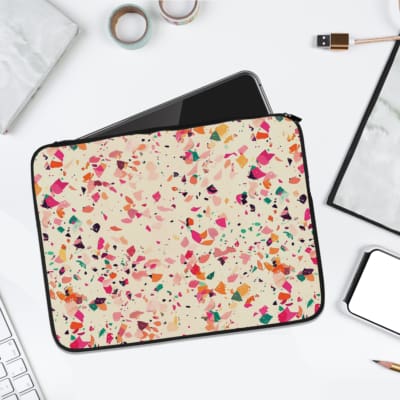 Laptop sleeve with a colorful terrazzo pattern in pink, orange, yellow, green, and black shapes on a white background, with a zip closure. laptop sleeve kept on a plain white background