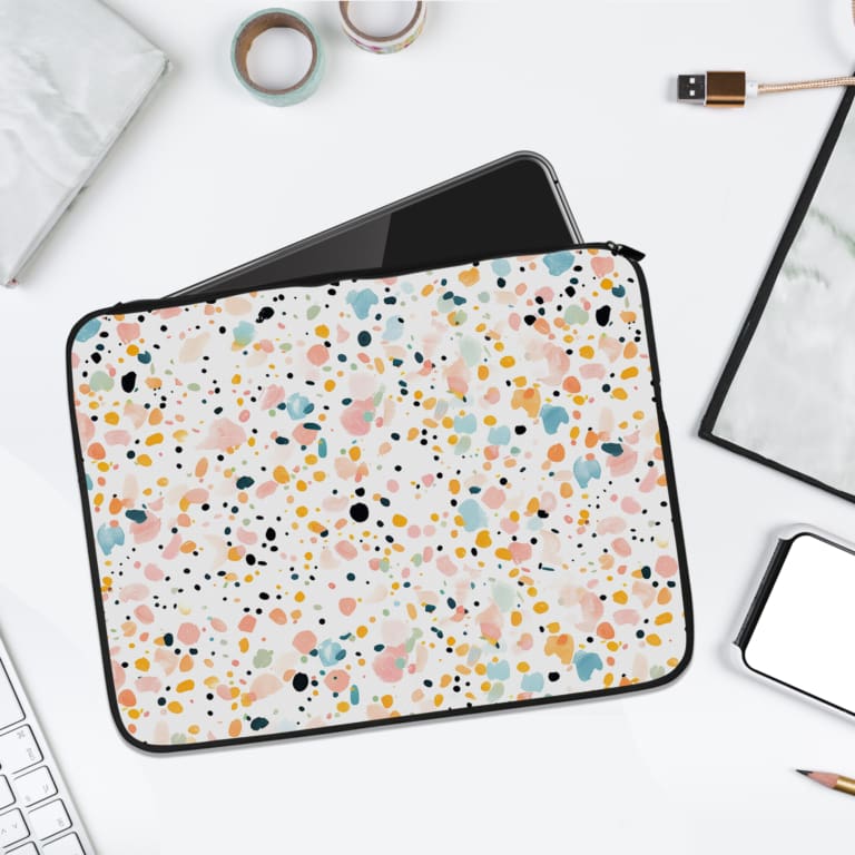 Laptop sleeve with a colorful speckled design in black, orange, blue, and yellow on a light background, featuring a secure zip closure. laptop sleeve kept on a plain white background