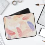 Laptop sleeve with a soft pastel feather design in pink, blue, purple, and orange on a light background, featuring a secure zip closure. laptop sleeve kept on a plain white background