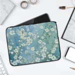 Blue floral laptop sleeve with white flower pattern, surrounded by notebooks, pen, and rings. laptop sleeve kept on a plain white background