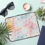 Colorful splatter paint design laptop sleeve with blue, orange, and pink splashes on a light background. the laptop sleeve on the table