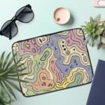 Laptop sleeve with topographic map design in pastel colors, featuring contour lines on a neutral background. the laptop sleeve on the table