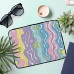 Retro-inspired laptop sleeve with wavy pastel stripes in pink, purple, yellow, green, and blue, covering the surface with a zip closure. the laptop sleeve on the table