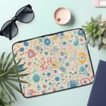 Laptop sleeve with a pastel bubble pattern in light blue, coral pink, and peach circles on a white background, secured with a zip closure. the laptop sleeve on the table