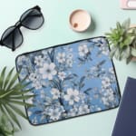 Elegant laptop sleeve with a blue background and white flowers with gray details, featuring small blossoms and leaves, secured with a zip. the laptop sleeve on the table