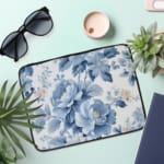 Laptop sleeve with a blue floral design, featuring light and dark blue flowers on a white background with a secure zip closure. the laptop sleeve on the table