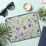 Laptop sleeve with purple floral design, featuring purple flowers and green leaves on a light background, with a secure zip closure. the laptop sleeve on the table