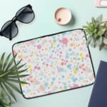 Laptop sleeve with colorful polka dots in pastel shades of pink, blue, yellow, and purple on a light background, with a secure zip closure. the laptop sleeve on the table