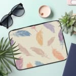 Laptop sleeve with a soft pastel feather design in pink, blue, purple, and orange on a light background, featuring a secure zip closure. the laptop sleeve on the table