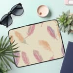 Infidu Pastel Feather Laptop Sleeve with a soft feather design in pastel shades on a light background, displayed on a white desk. the laptop sleeve on the table