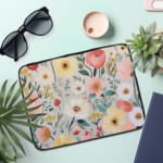 Infidu Vibrant Floral Laptop Sleeve with red, yellow, pink, and white flowers against a light background on a white desk. the laptop sleeve on the table