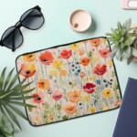 Colorful floral laptop sleeve with red, pink, yellow, and orange flowers on a light background. the laptop sleeve on the table