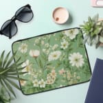 Floral laptop sleeve with white flowers and green leaves on a soft green background. the laptop sleeve on the table