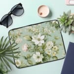 Floral laptop sleeve with white flowers and green leaves on a soft green background. the laptop sleeve on the table