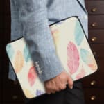 Infidu Pastel Feather Laptop Sleeve with soft fabric in pink, blue, and orange shades, featuring a zip closure for secure laptop protection. the person holding the sleeve