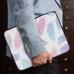 Infidu Pastel Feather Laptop Sleeve with soft fabric in pink, blue, and purple shades, featuring a zip closure for secure laptop protection. the person holding the sleeve