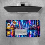 Infidu Neon City Street Desk Pad features a vibrant nighttime city scene with neon lights reflecting on a wet street, perfect for an energetic workspace. A desk pad under the computer