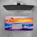 Infidu Serene Sunset Wave Design Desk Pad features colorful soft waves in blue, purple, and pink with a yellow and orange sunset. A desk pad under the computer